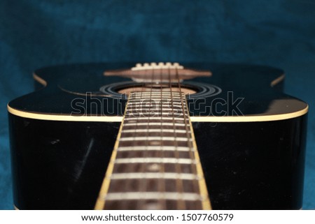 Black guitar on blue background close-up. Guitar neck and strings.