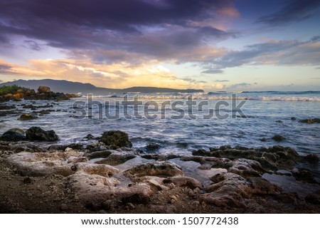 Sunrise on Ocean with rocks on Sandy Beach and colorful Sky in background.