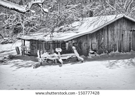 A black and white rural scene photograph of vintage barn on a bright sunny winter morning after a fresh snow fall. 