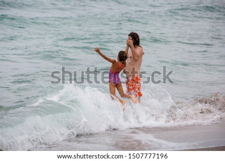 Father and daughter playing in water. Jumping on waves by the seaside. Summer family fun.