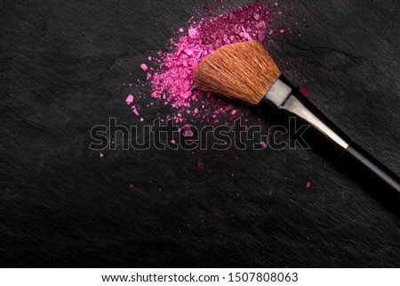 Make-up brush with vibrant crushed cosmetics, shot from the top on a black background with a place for text, a beauty design template for a makeup artist's business card