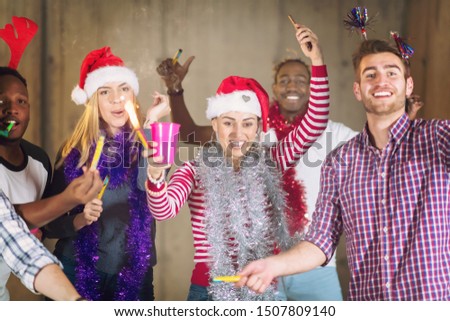 multiethnic group of young happy casual business people dancing with sparklers and having fun while celebrating new year eve in front of concrete wall at new startup office