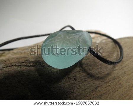 Sea foam sea glass pendant hangs on black cord and lies on brown driftwood. Recycling nature jewelry concept. Royalty-Free Stock Photo #1507857032