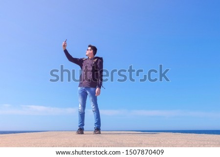 Young man tourist travel blogger make selfie on smartphone at sea pier, low angle view. Guy blogger work make photo on phone create content for social media, modern job. Travel journey trip sunny day.