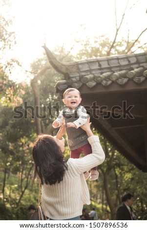 An Asian mother throws her laughing baby girl up in the air while playing near a traditional Chinese temple in Ritan Park, Chaoyang district, Beijing, China