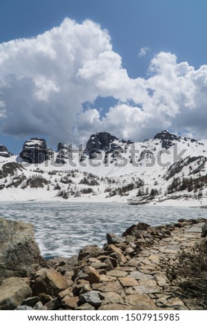 View of the beautiful Allos frozen lake nature, moutains, peak and white snow, ice on pure water, rocks, blue sky with clouds, spring, Mercantour national park, Alps, France.