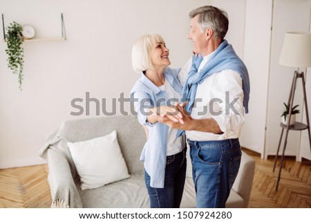 Happy mature couple dancing slow ballroom dance in the living room and looking at each other, free space