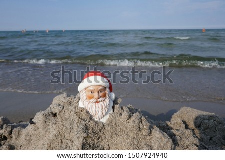 Christmas by the sea. Have fun at the beach holiday with Santa Claus. Little garden gnome in Santa Claus costume goes on vacation in the tropics and takes a sand bath (Not copyrighted)