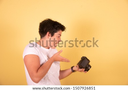 Young woman in white shirt taking photos with a camnera in a yellow background