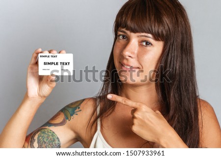 Finance and Bank cards. A young woman with tattoos smiling and holds a Bank card and points at it with her finger. Close up