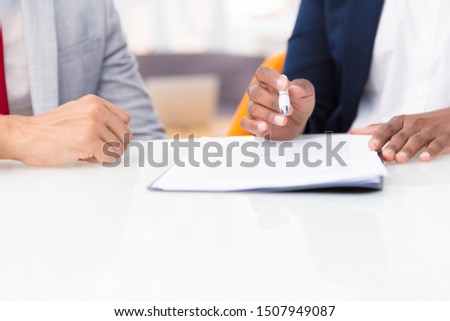 Two business colleagues studying contract. Business man and woman sitting at office table, holding pen and reading documents together. Paper expertise concept. Cropped view