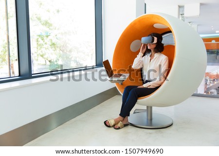 Female customer testing VR simulator. Woman in office clothes and virtual reality headset sitting in interactive chair with laptop and touching device. VR engineering concept Royalty-Free Stock Photo #1507949690