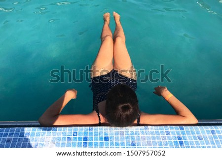 Girl in the pool outdoors. Leaned on board the pool. Smiling, sunglasses on his head.