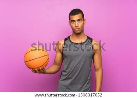 Young sport man with ball of basketball over isolated purple wall with sad expression
