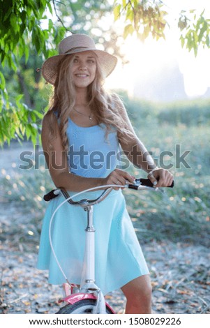 beautiful young girl holding her bike hands behind the wheel smiling at the background of the Park and nature
