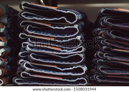 Jeans are stacked in piles in a store. Jeans are stacked on a shelf. Size range