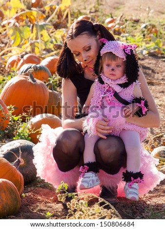 Toddler and her mother dressed up in cute costumes at the pumpkin patch.