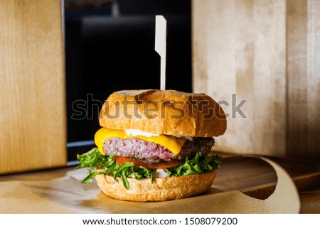 Meat burger with vegetables and cheese close-up on a wooden background in a restaurant on a table with a wooden skewer.