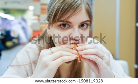 Close up portrait of a hungry young woman eating burger in restaurant. Student consume fast food. 