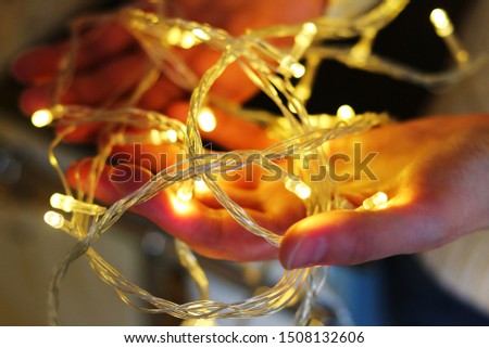 Blurred Christmas garland in hands. Blurred festive gold garland lights in hands. Holiday postcard / picture with space for text.