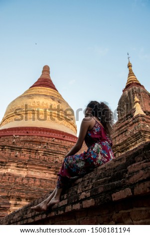Vertical picture of young woman sitting on the walls of the architectonic Dhammayazika Temple, a beautiful buddhist pagoda in Bagan in Myanmar