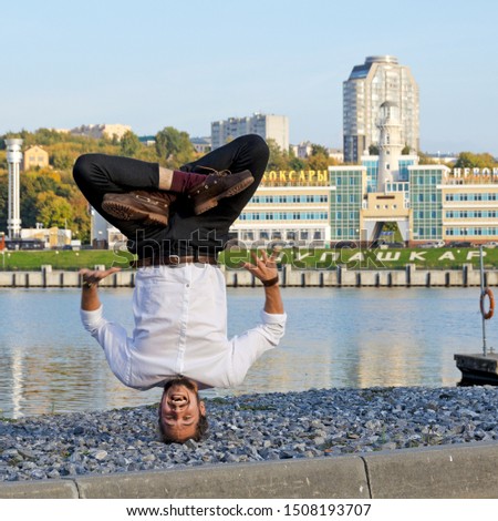 Translation: "Cheboksary. Name of the city in Russian and Chuvash languages."Upside down, as if a guy fell from the sky with his head into the ground, a guy poses against the background of the city. T