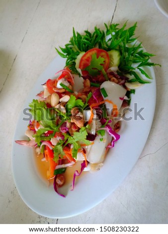 Various seafood spicy salad in white plate, decorate with herbal local organic vegetables, cucumber, tomato and Polyscias leaves, overhead view vertical picture, Asian tropical food in iceland of Thai