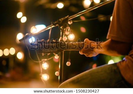 Rear view of the man sitting play acoustic guitar on the outdoor concert with a microphone stand in the front, musical concept. Royalty-Free Stock Photo #1508230427