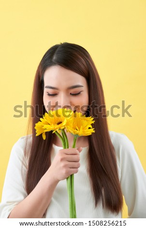 young woman smelling sunflowers on the yellow background