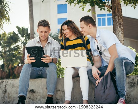 Happy university student using laptop together outside building with natural light.