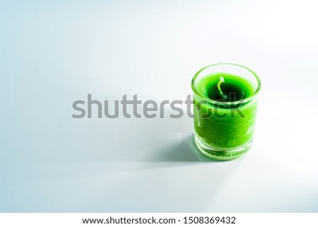 Green candle in clear glass By a shining light on the White Blackground