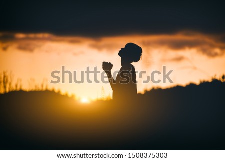 Young christian sitting and pray to God at sunset background. christian silhouette concept.
