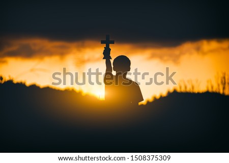 Young christian holding and lift the Cross at sunset background. christian silhouette concept.