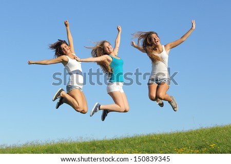 Group of three teenager girls jumping on the grass with the sky in the background            
