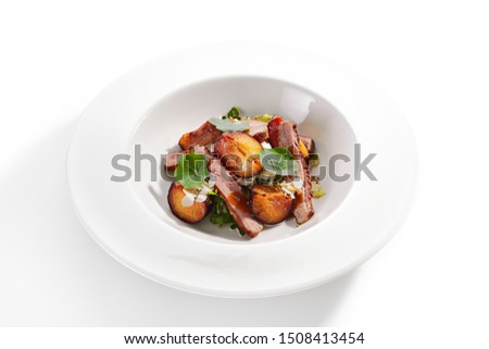 Exquisite serving salad with roasted duck breast, baked pear and strachatella cheese on white restaurant plate isolated. High cuisine restaurent dish with delicious grilled meat and fruits closeup