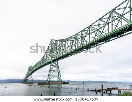 Truss arched long Astoriaâ€“Megler bridge in Astoria city at the mouth of the Columbia River at the Pacific ocean and an old trolley on rails that go into the water and the remains of a rotted marina