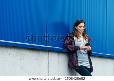 horizontal photo of a happy young brunette woman with purple sport wear using the smartphone with a blue background