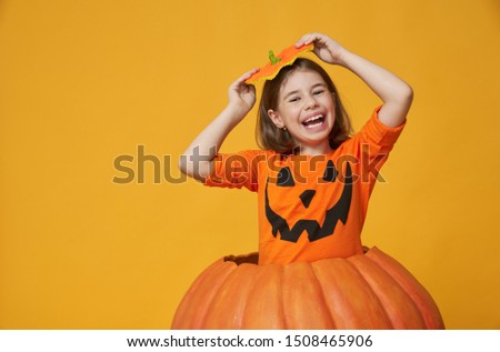 Happy Halloween! Cute little girl in pumpkin costume on yellow background.   