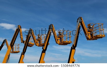 Aerial work platforms lined up against blue sky with clouds Royalty-Free Stock Photo #1508469776