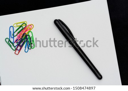 
Paper clip and pen on a white sheet with black background