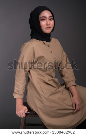 Fashionable young woman in black jeans, long sleeves dress and hijab isolated on grey background. Studio fashion and beauty concept.