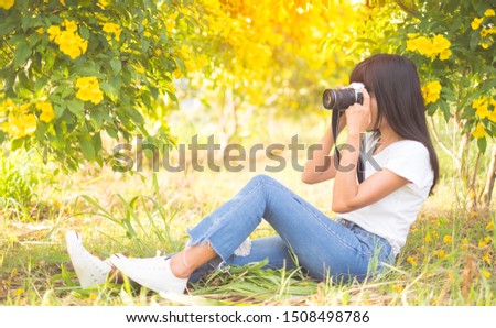 Asian women photographer covering her face on  Yellow trumpet-flower background.