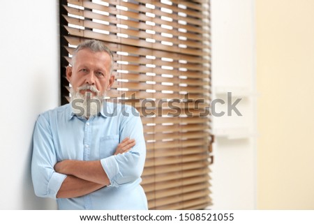 Portrait of handsome mature man near window with blinds