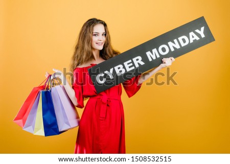 smiling pretty girl has cyber monday sign with colorful shopping bags isolated over yellow