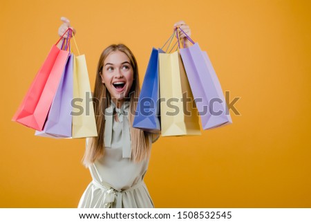 beautiful happy smiling blonde girl with colorful shopping bags isolated over yellow
