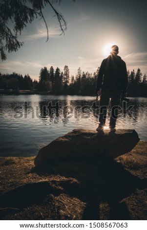 Sun Set with  Person on a Rock next to a Lake in the Forest