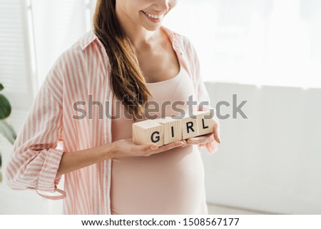 cropped view of smiling pregnant woman holding wooden blocks with word