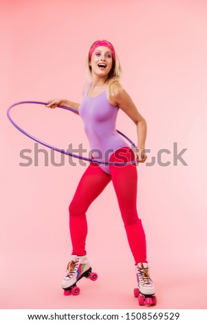 Image of smiling blonde woman in retro roller skates doing exercise with hula hoop isolated over pink background