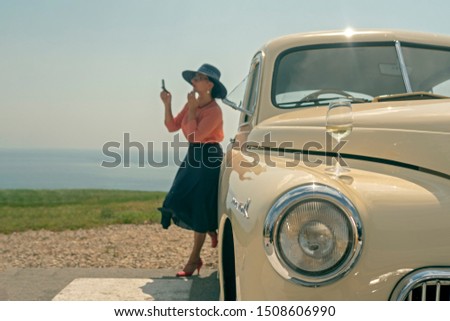 A woman in a hat adjusts makeup at a vintage car. Travel, vacation