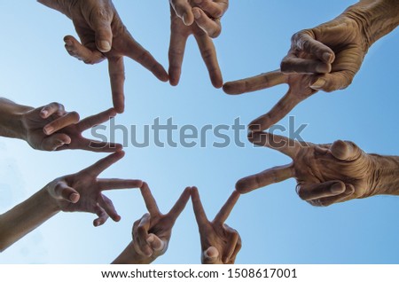 Lot of people makes victory sign with her hands in the form of a star  - background blue sky with sun